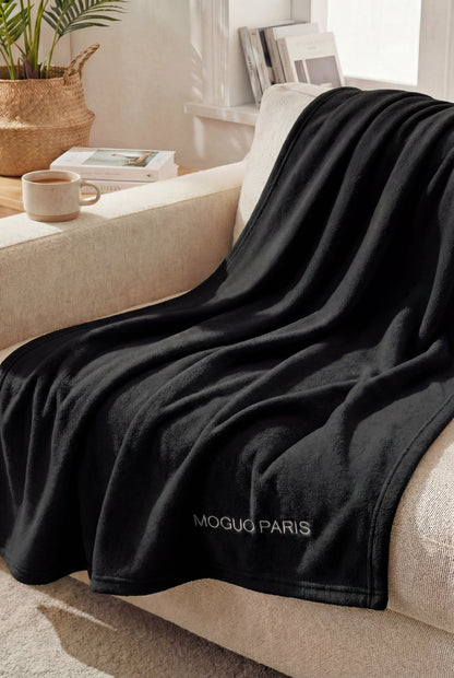 Mannequin femme profitant d'un moment cocooning sous le plaid polaire noir taille XL sur un canapé design.