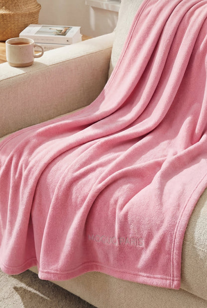 Femme se relaxant sur un canapé, enveloppée dans le grand plaid rose cocooning XL.