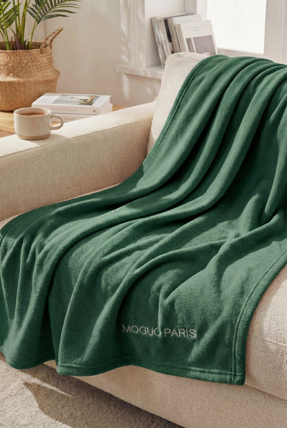 Femme se relaxant sur un canapé, enveloppée dans le grand plaid vert confortable taille XL.